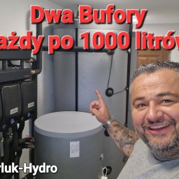 KARLUK-HYDRO - Uśmiechnięty mężczyzna z tatuażem na ramieniu wskazuje na dwa szare bufory ciepła o pojemności 1000 litrów każdy, obok widoczne czarne moduły instalacyjne z manometrami, na zdjęciu nałożony napis...
