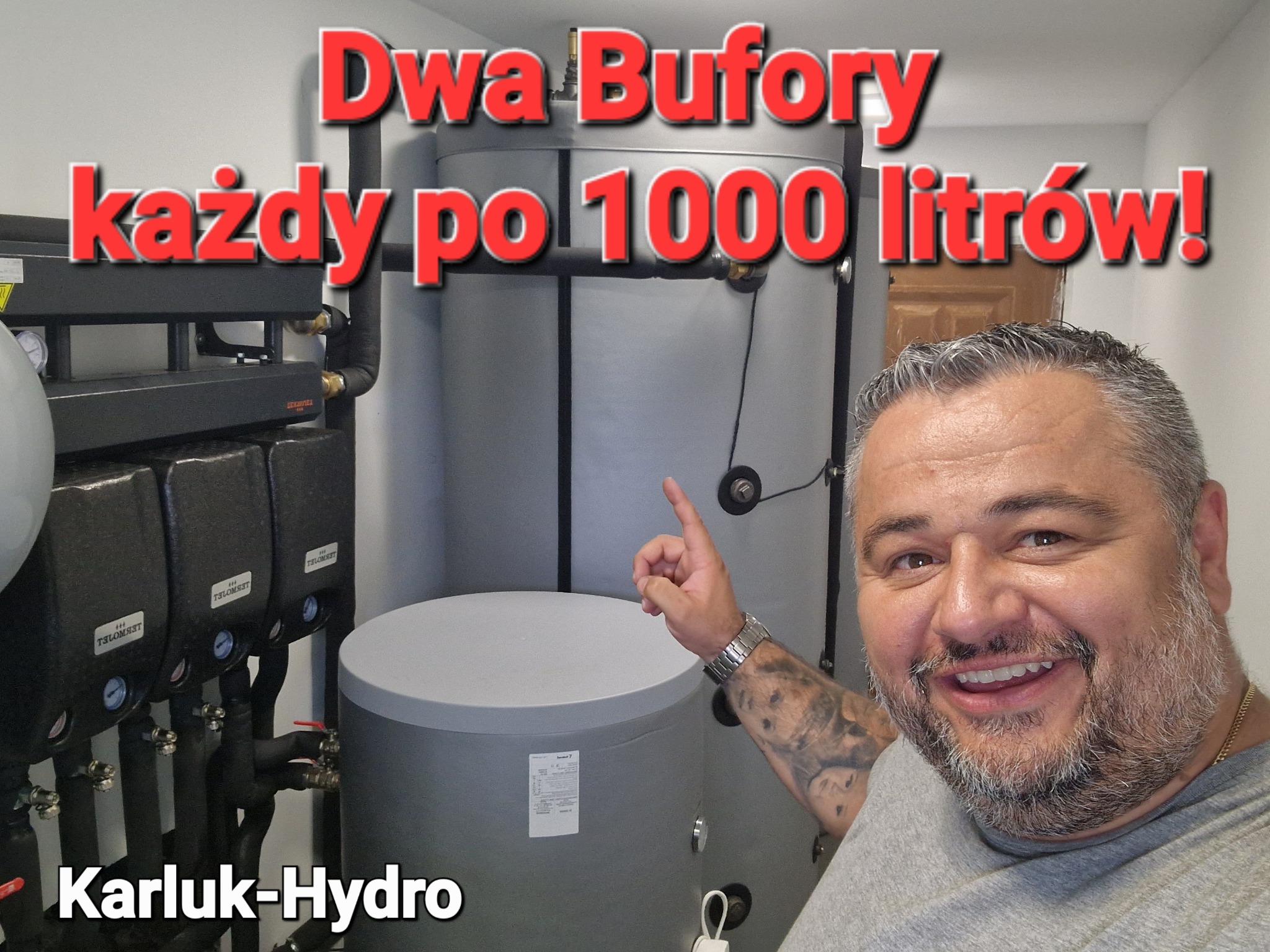 Uśmiechnięty mężczyzna z tatuażem na ramieniu wskazuje na dwa szare bufory ciepła o pojemności 1000 litrów każdy, obok widoczne czarne moduły instalacyjne z manometrami, na zdjęciu nałożony napis...