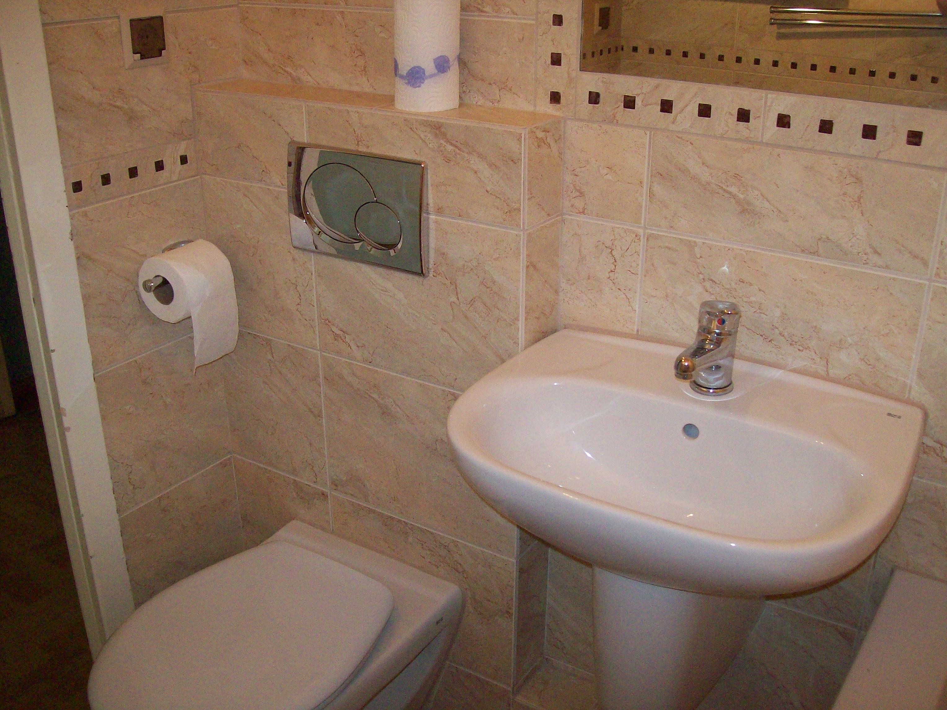 Umywalka na postumencie, toaleta i marmurowe płytki zdobione małymi kwadratami w wyremontowanej łazience.