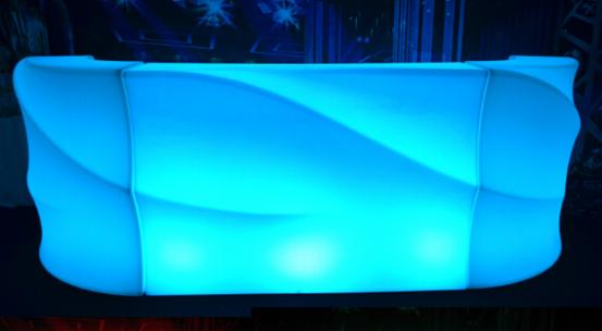 Podświetlany bar o falistym kształcie, świecący na niebiesko, z trzema punktami świetlnymi na froncie, ustawiony na ciemnym tle.