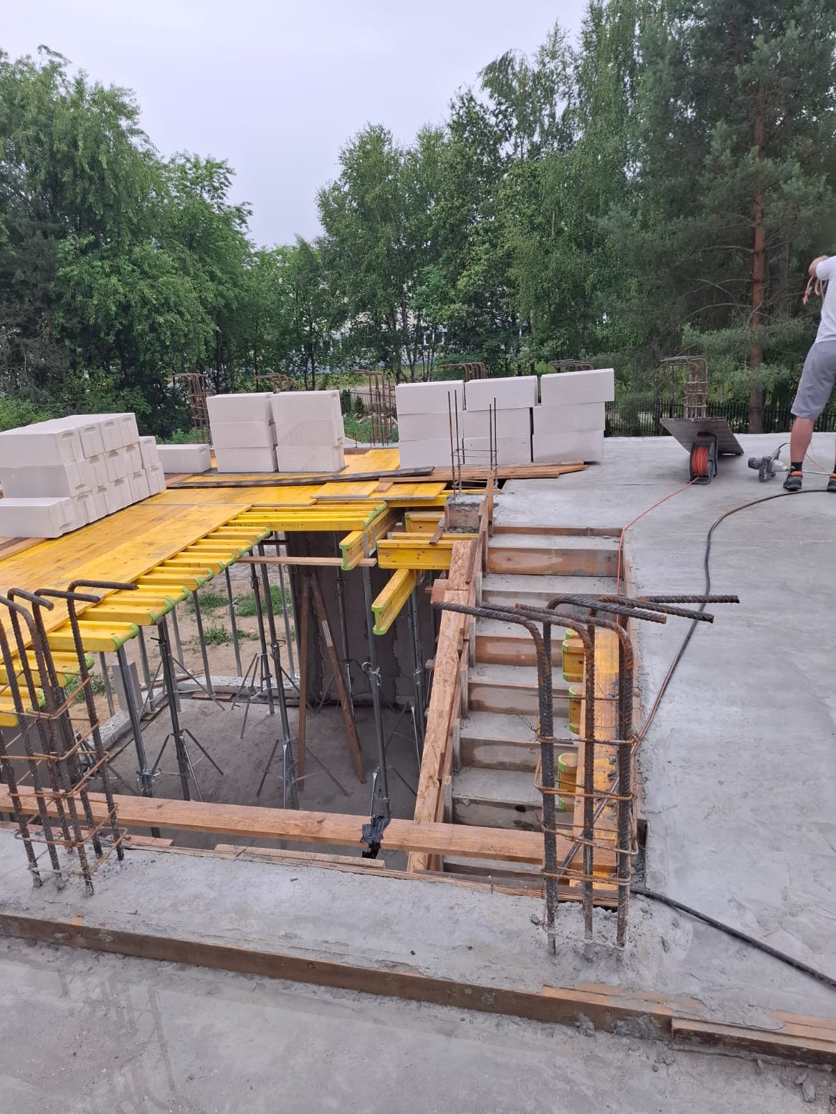 Fundamenty domu w trakcie budowy: zbrojenie, szalunki, bloczki betonowe. Widoczne elementy konstrukcyjne i przygotowanie do dalszych prac budowlanych. Ujęcie z góry.