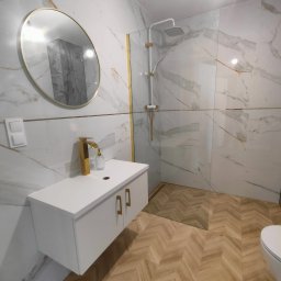 MED-BUD - Elegancka łazienka po remoncie: białe marmurowe płytki z złotymi akcentami, armatura w kolorze złota, wzór jodełki na podłodze, kabina prysznicowa ze szkła.