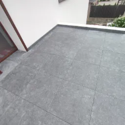 Szare płytki na tarasie wentylowanym z wklejonymi cokołami, widok z góry, jasne ściany, okno. Detal wykończenia.