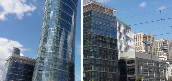 Dwa nowoczesne biurowce ze szklanymi fasadami pod błękitnym niebem z chmurami, widoczne linie tramwajowe.