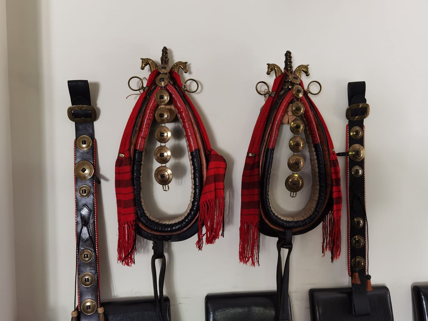 Uprzęże końskie z elementami skórzanymi i dzwonkami, wiszące na ścianie w Toruniu, z widocznymi detalami zdobniczymi i metalowymi okuciami.