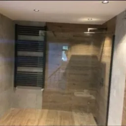 Nowoczesna łazienka z kabiną prysznicową typu walk-in, grzejnikiem drabinkowym i drewnopodobnymi płytkami na ścianach i podłodze.