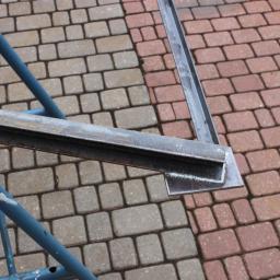 PRZEDSIĘBIORSTWO PRODUKCYJNO-USŁUGOWE ARMIKS SPÓŁKA Z OGRANICZONĄ ODPOWIEDZIALNOŚCIĄ - Metalowa konstrukcja spawana z profili stalowych, widoczna spoina na tle kostki brukowej w dwóch odcieniach.