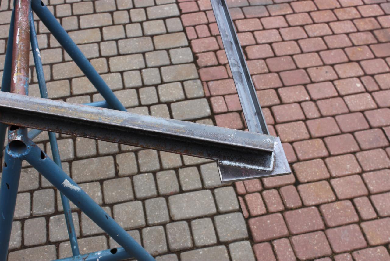 Metalowa konstrukcja spawana z profili stalowych, widoczna spoina na tle kostki brukowej w dwóch odcieniach.