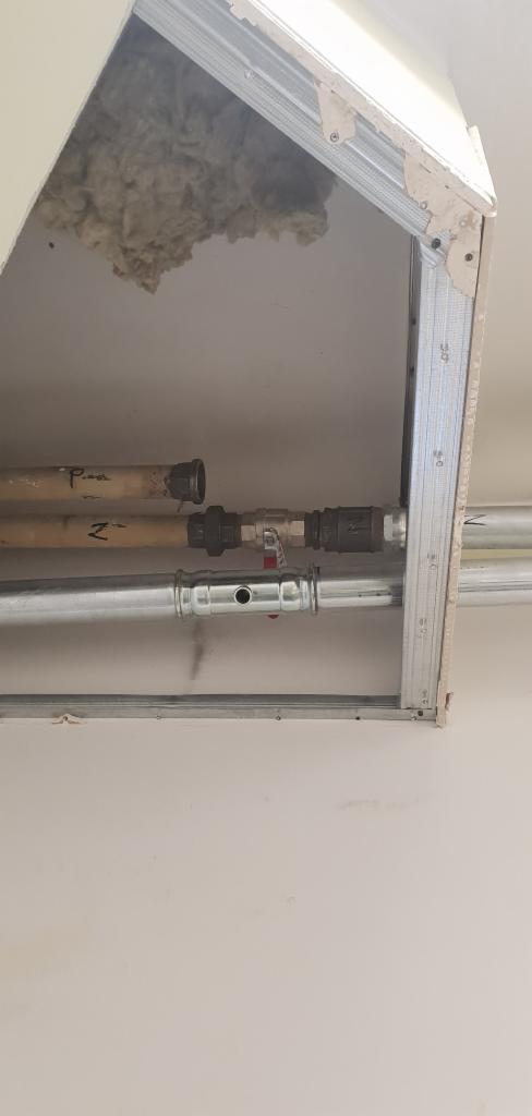 Rury instalacyjne, miedziane i stalowe, podwieszone pod sufitem podwieszanym z widoczną wełną mineralną w przestrzeni nad sufitem.