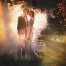 Fotograf ślubny - Para młoda w objęciach, pocałunek w otoczeniu dymu i promieni słonecznych, plenerowa sesja ślubna.