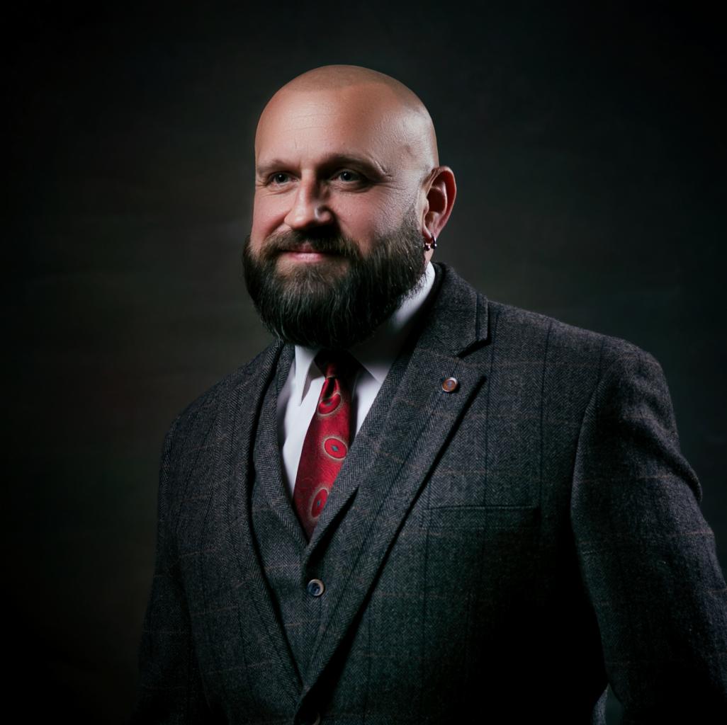 Portret brodatego mężczyzny w tweedowym garniturze i czerwonym krawacie, z kolczykiem w uchu, wykonany w studiu w Skarżysko-Kamiennej.