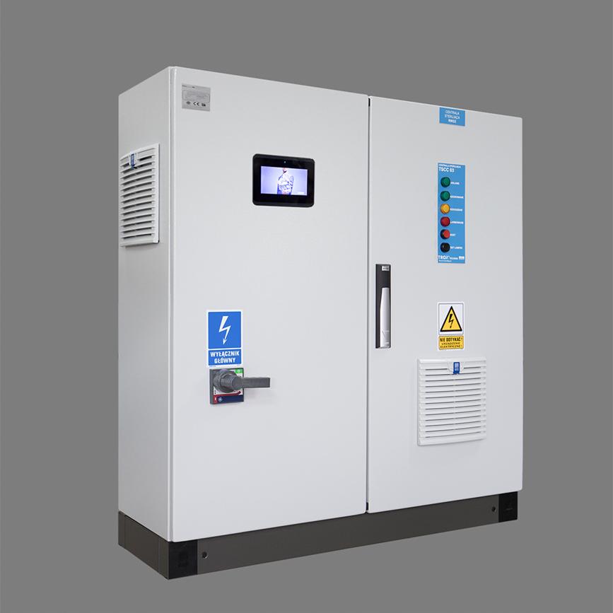 Dwudrzwiowa, biała szafa sterownicza z wyświetlaczem i oznaczeniami ostrzegawczymi, umieszczona na czarnym cokole.