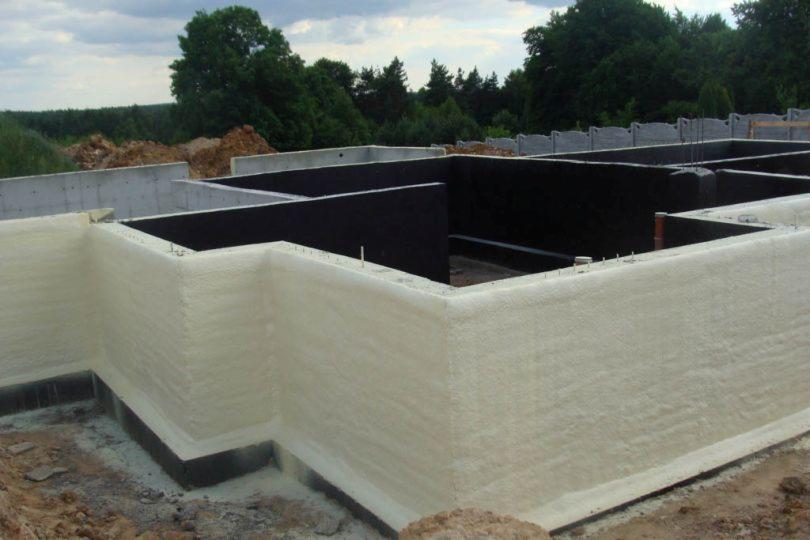 Izolacja fundamentów budynku mieszkalnego, widoczna pianka poliuretanowa na ścianach fundamentowych oraz hydroizolacja pionowa wewnątrz wykopu.