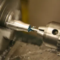 Tokarka w trakcie obróbki metalu, wióry i chłodziwo widoczne na obrabianym elemencie, zbliżenie na proces toczenia.