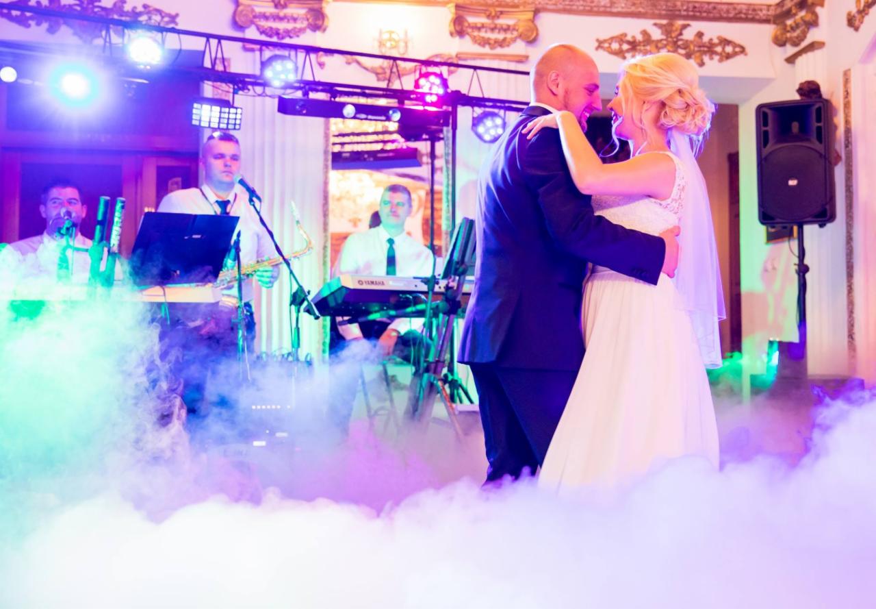 Para młoda tańczy w objęciach na parkiecie wypełnionym dymem, w tle zespół muzyczny z saksofonem i instrumentami klawiszowymi.
