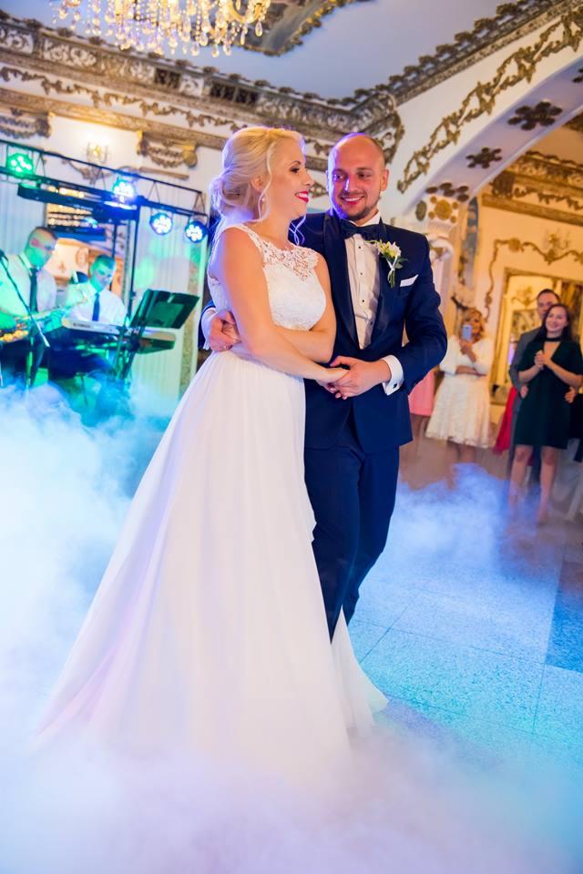 Para młoda w tańcu podczas wesela, w tle zespół muzyczny i goście, parkiet spowity sztucznym dymem.