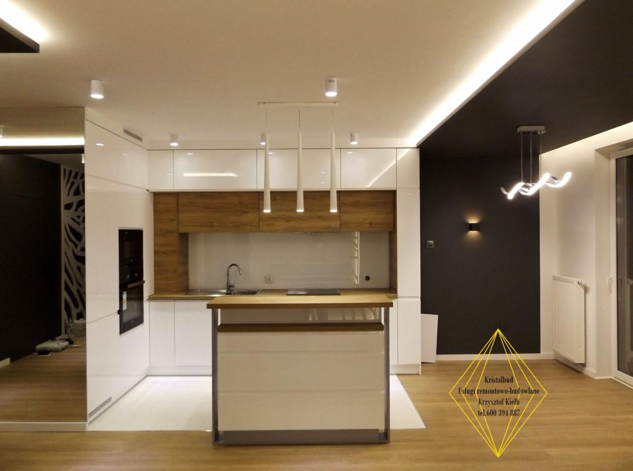 Nowoczesna kuchnia z wyspą, białe lakierowane szafki z drewnianymi akcentami, wiszące lampy tubowe, czarny sufit z oświetleniem LED, podłoga imitująca drewno, minimalistyczny design.