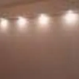 Gładka, jasna ściana oświetlona rzędem punktowych lamp sufitowych, tworzących ciepłą, rozproszoną poświatę.