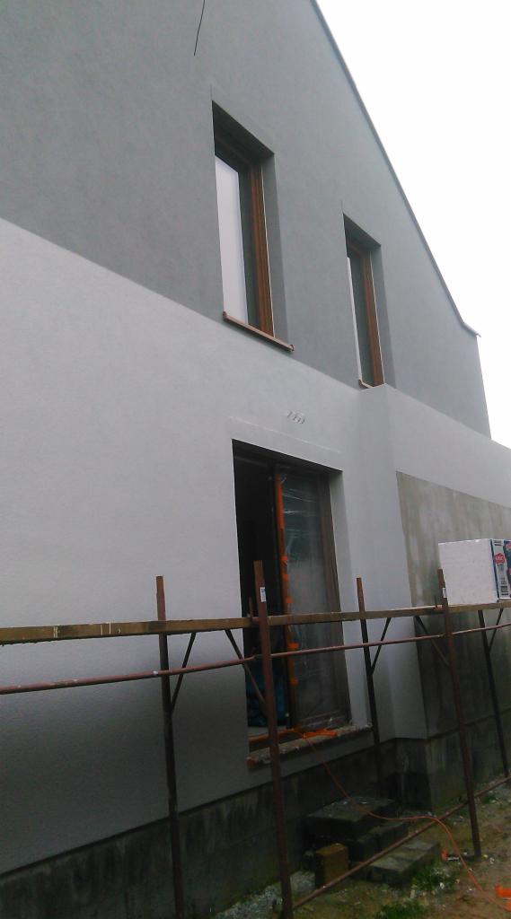 Dwukolorowa elewacja domu w Rozprzy w trakcie wykonywania, widoczne rusztowania i materiały budowlane.