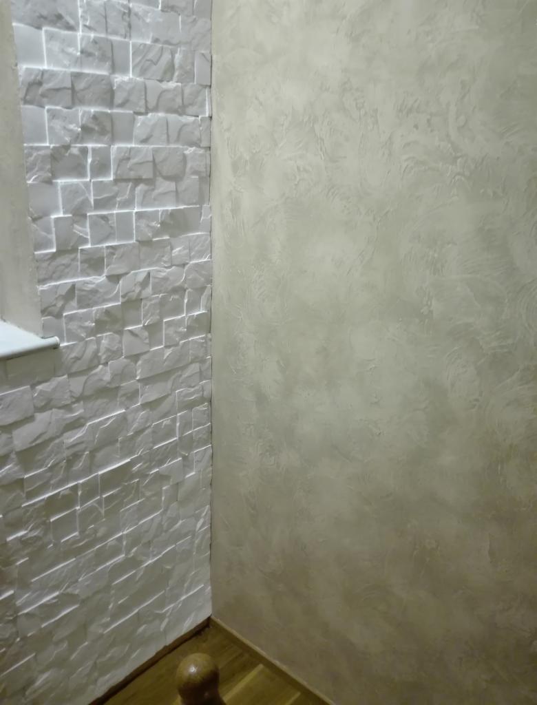 Dekoracyjne wykończenie wnętrza: ściana z białej, trójwymiarowej okładziny imitującej kamień i ściana z beżową, wzorzystą fakturą.