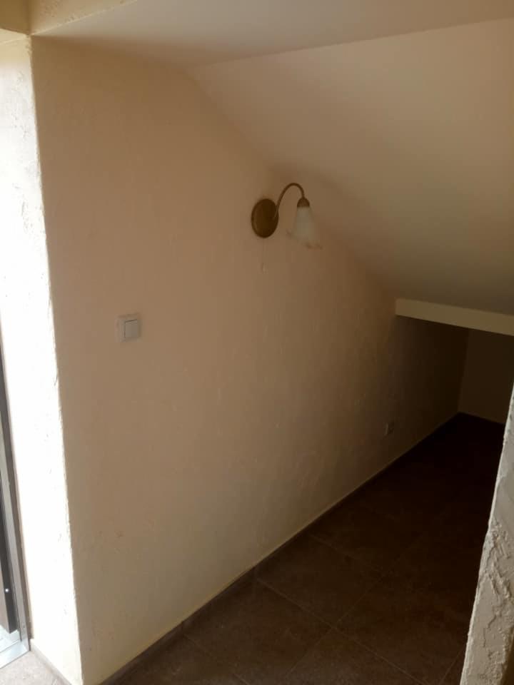 Poddasze po remoncie: beżowe ściany, brązowa terakota, kinkiet z białym kloszem, widoczny włącznik na ścianie.