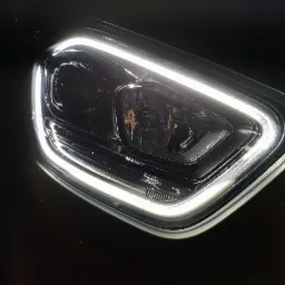 Reflektor samochodowy z jasnymi światłami LED, widoczny z bliska pod kątem, na ciemnym tle.