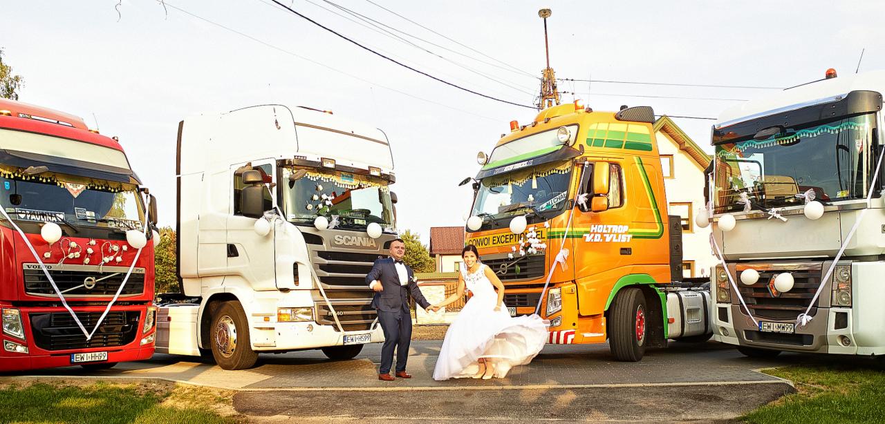 Para młoda trzymająca się za ręce pozuje na tle czterech udekorowanych ciężarówek Volvo, Scania, Holtrop i Renault w dniu ślubu.
