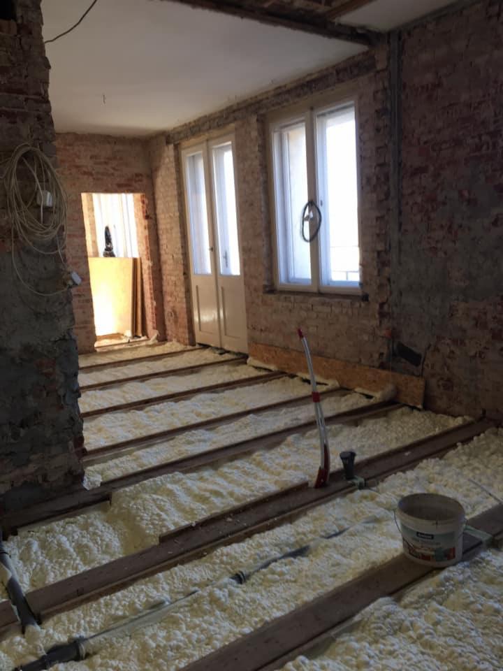 Podłoga w trakcie ocieplania pianką w Czarnożyłach, widoczne drewniane legary i wypełniająca je piana, ściany z surowej cegły.