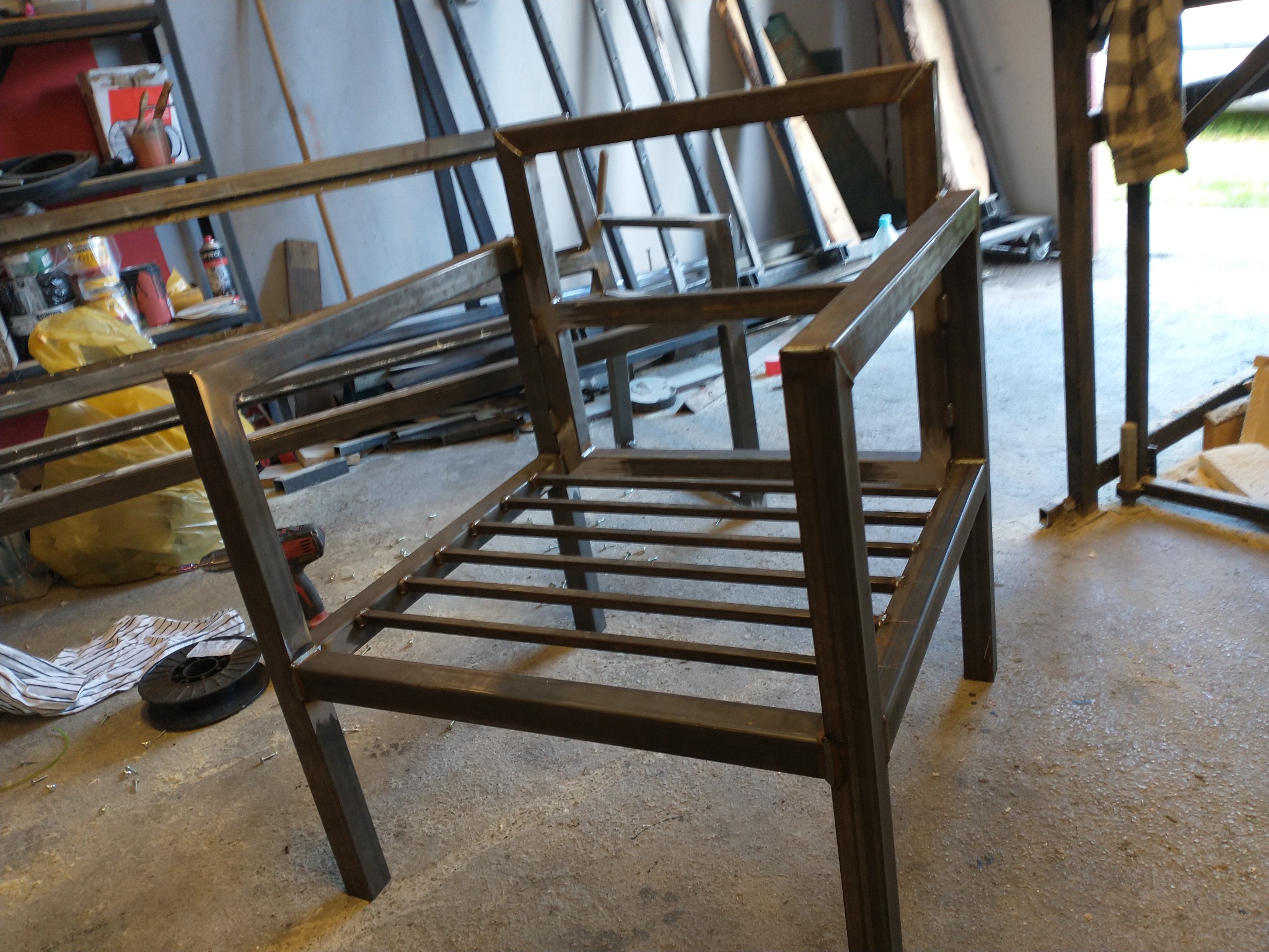 Metalowy szkielet krzesła spawany z profili, widoczne ślady po spawaniu, w tle warsztat.