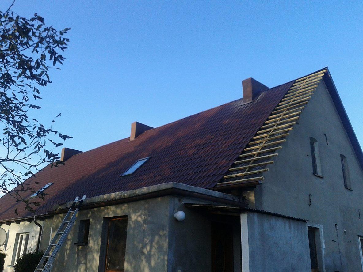 Dom jednorodzinny z częściowo zdjętym pokryciem dachowym, widoczne łaty pod nowe pokrycie, komin i okno dachowe, drabina oparta o budynek.