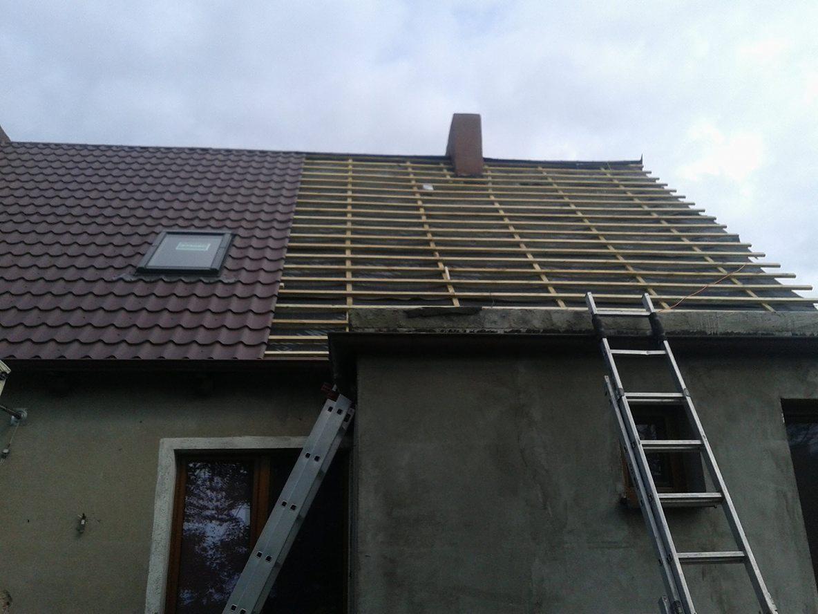 Dom w trakcie remontu dachu: część pokryta brązową dachówką, część z widoczną drewnianą konstrukcją i kominem, drabiny opierają się o ściany budynku.