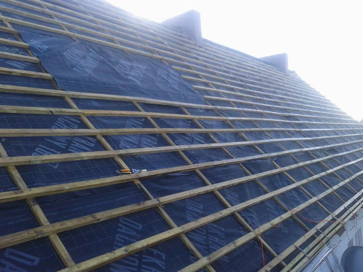 Konstrukcja dachu z łatami i membraną dachową, widok z dołu pod kątem, częściowo pokryta, z narzędziami na membranie.