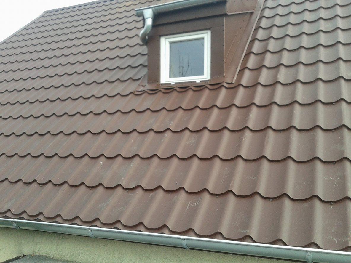 Brązowy dach z blachy trapezowej z oknem dachowym i systemem rynnowym, widok z dołu.