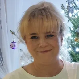 Portret uśmiechniętej kobiety z blond włosami na tle choinki z bombkami, być może właścicielka firmy z branży odnawialnych źródeł energii.