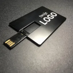 Czarny, metalowy pendrive w kształcie karty kredytowej z napisem 'twoje LOGO' w kolorze białym, leżący na ciemnoszarym, matowym tle.