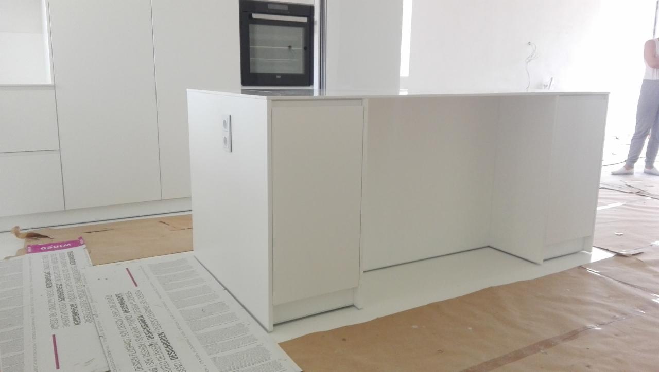 Montaż białej wyspy kuchennej z piekarnikiem w tle, widoczne zabezpieczenia podłogi podczas prac.