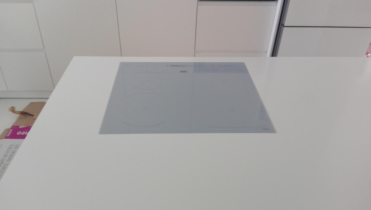 Biały blat kuchenny z wbudowaną płytą indukcyjną, widoczne białe szafki kuchenne w tle, obok kartonowe opakowanie.