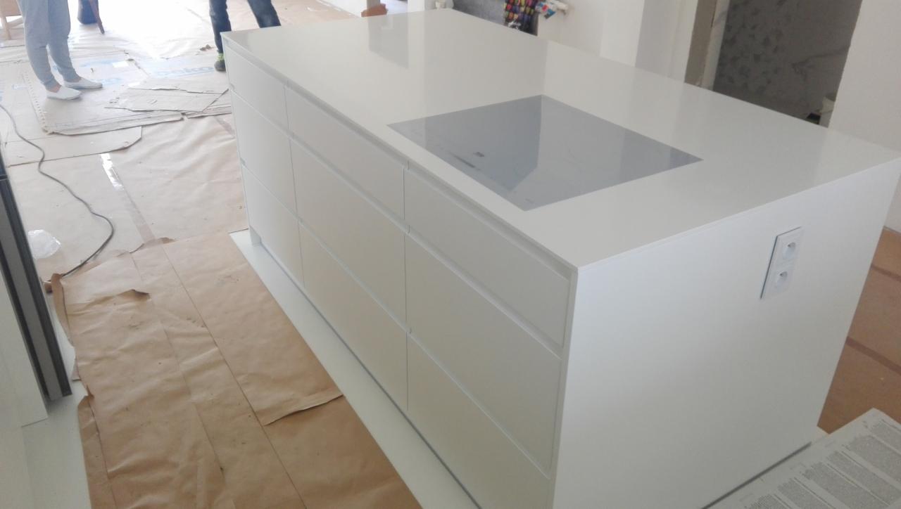 Biała wyspa kuchenna z wbudowaną płytą indukcyjną, widoczne zabezpieczenia podłogi podczas montażu.
