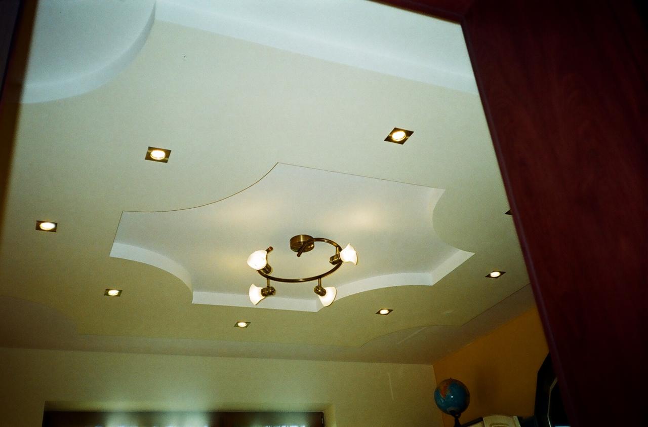 Sufit podwieszany z dekoracyjnym wzorem i oświetleniem punktowym oraz centralną lampą z czterema kloszami w kolorze złota.