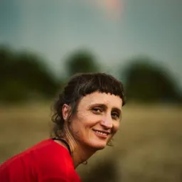 Uśmiechnięta kobieta w czerwonej koszulce na tle pola i tęczy na niebie. Portret w naturalnym oświetleniu.