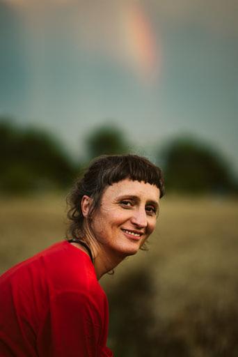 Uśmiechnięta kobieta w czerwonej koszulce na tle pola i tęczy na niebie. Portret w naturalnym oświetleniu.