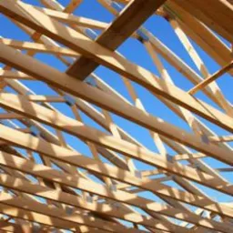 Konstrukcja drewniana więźby dachowej na tle błękitnego nieba, widok od dołu.