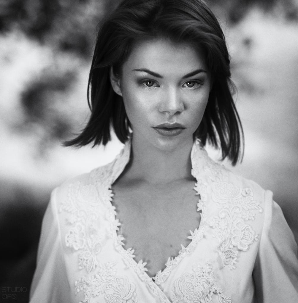 Portret kobiety w białej bluzce z koronkowym wykończeniem, czarno-białe zdjęcie z delikatnym rozmyciem tła.