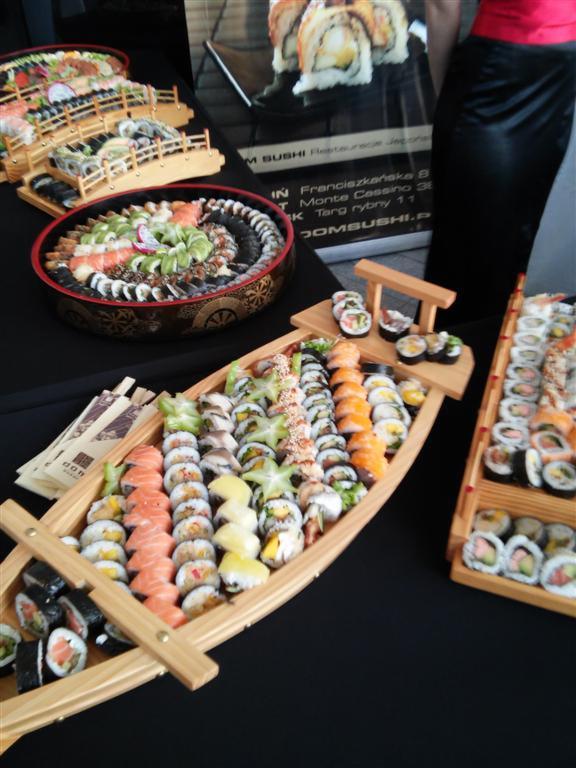 Dekoracyjnie podane sushi: różnorodne rolki ułożone w drewnianych naczyniach w kształcie łodzi i okręgów, z widocznymi gwiazdami karamboli i pałeczkami.