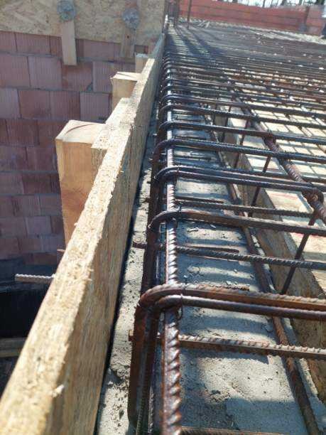 Zbrojenie stropu w szalunku z desek, widoczne pręty zbrojeniowe ułożone w siatkę, przygotowane do zalania betonem. Ceglany mur w tle.