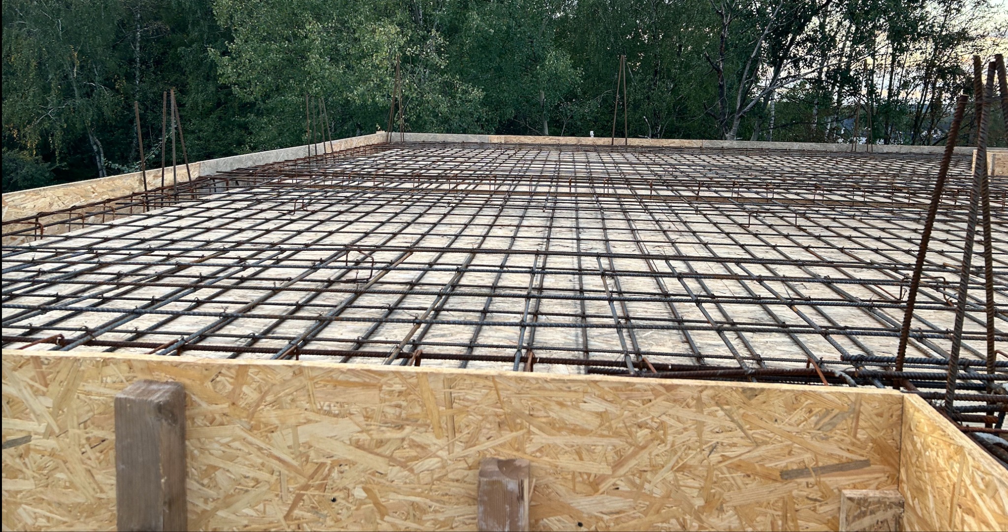 Zbrojenie płyty fundamentowej z siatką stalową na szalunku z płyty OSB, widok z góry na tle zieleni. Etap budowy domu jednorodzinnego.