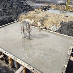 SVAN Sp. z o.o. - Świeżo wylany fundament pod budowę z wystającą zbrojoną konstrukcją i drewnianym szalunkiem, widok z góry na plac budowy.