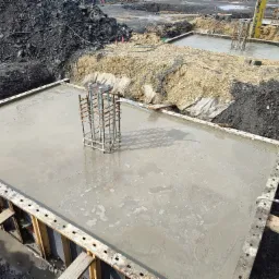 Świeżo wylany fundament pod budowę z wystającą zbrojoną konstrukcją i drewnianym szalunkiem, widok z góry na plac budowy.