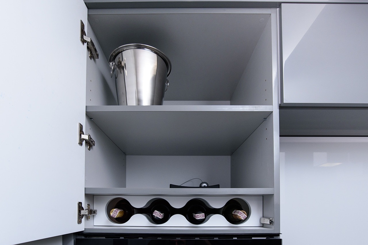 Szara szafka kuchenna z otwartymi drzwiczkami, na półkach wiaderko na lód i stojak na cztery butelki wina.