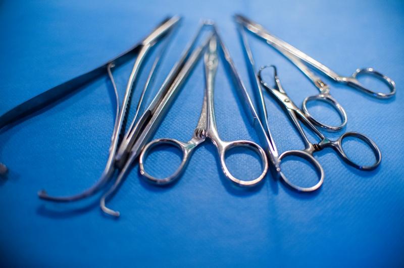 Zestaw sterylnych narzędzi chirurgicznych ze stali nierdzewnej ułożonych na niebieskim podkładzie, w tym kleszcze, pęsety i nożyczki.